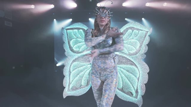 Beautiful girl in butterfly costume with colored lights performs on stage. Modern dance show.