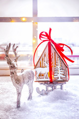 Christmas decor: deer carries on a sleigh a gift dream house. Comfort, candles, Christmas wreath on the window sill. Winter mood, festive New Year's decoration.