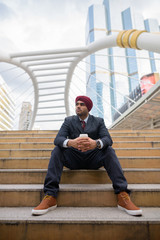 Indian businessman sitting outdoors in city while thinking