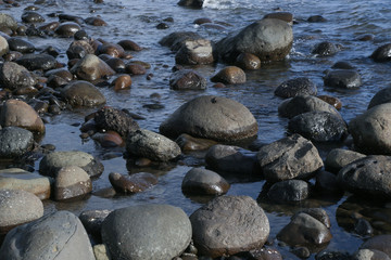Fototapeta na wymiar Big smooth black beach stones in the water