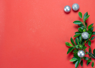 Red Christmas paper background decorated with green leaves and glitter silver ornament balls