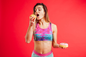 Portrait of a young woman choosing between  appel and a donut isolated over white background