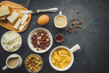 cornflakes, coffee, cottage cheese, bread, butter, eggs, jam and other ingredients for breakfast on a dark background. Top view with copy space