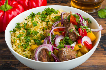 Big white bowl with beef cooked with vegetables, bulgur, red onion and fresh parsley, close-up