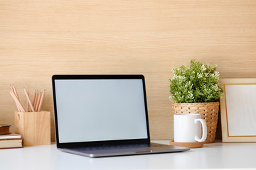 Close-up mockup laptop on white table. books, coffee, pencil. In the background a wood wall and house plants. Empty workplace.