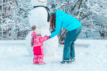 mother with daughter playing outside in winter time. making snowman