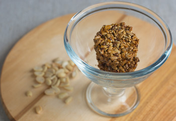 Glass bowl with roasted kozinaki from sunflower seeds on wooden board. Front view.