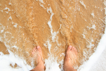 Top view of a man's leg standing on the sand and lapped by the ocean waves