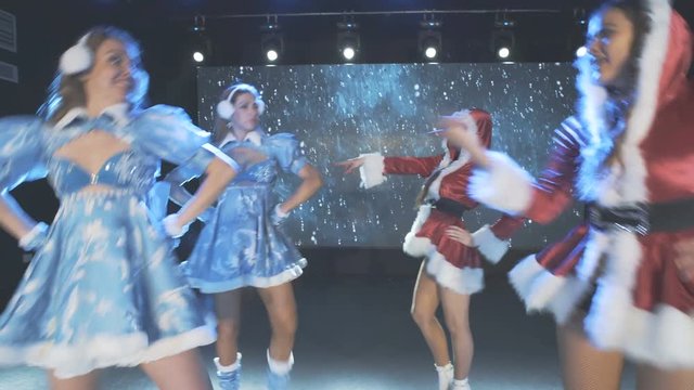 Beautiful cheerful girls in Christmas costumes perform on a stage. Dance show.