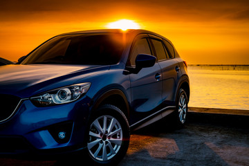 Fototapeta na wymiar Front view blue compact SUV car with sport and modern design parked on concrete road by the sea at sunset. Electric car technology and business. Hybrid auto and automotive. Tropical road trip travel.