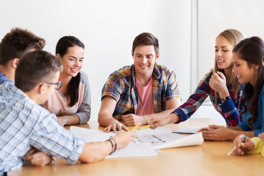 education, architecture and people concept - group of smiling students with blueprint meeting indoors