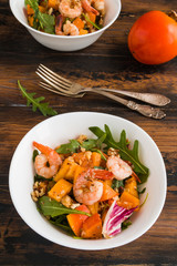 Light fruit salad with fried prawns, persimmon, arugula and walnuts in white bowls on wooden rustic table