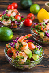 Mexican salad with fried shrimps, fresh avocado, cherry tomatoes, coriander and red cabbage in glass bowls on wooden rustic table