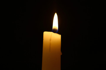 tiny paraffin glowing yellow candle with bright fire on the black background.