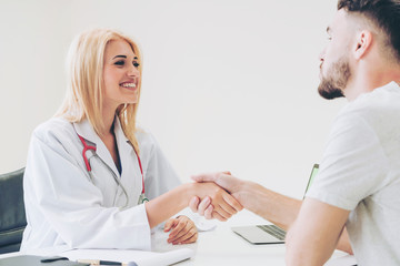 Woman doctor doing handshake with male patient in hospital office room. Healthcare and medical...