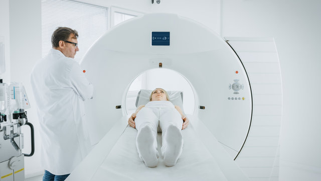 In Medical Laboratory Male Radiologist Controls MRI or CT or PET Scan with Female Patient Undergoing Procedure. Doctor Conducts Emergency Scanning with Advanced Medical Technologies. 