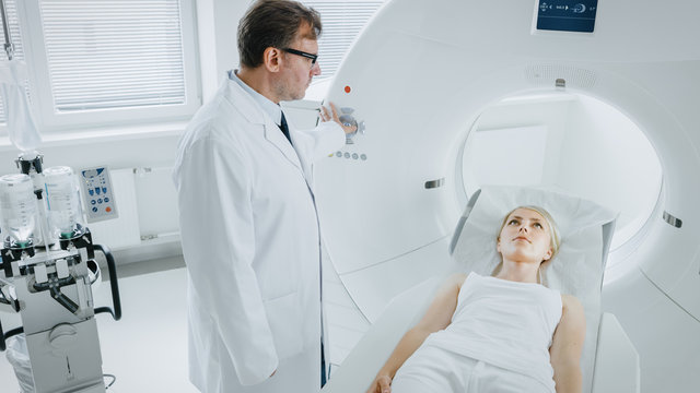 In Medical Laboratory Male Radiologist Controls MRI or CT or PET Scan with Female Patient Undergoing Procedure. High-Tech Modern Medical Equipment.