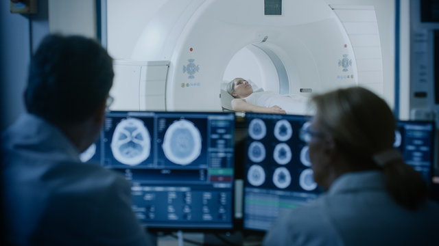 In Medical Laboratory Patient Undergoes MRI or CT Scan Process under Supervision of Doctor and Radiologist in Control Room, They Watche Procedure and Monitors Brain Activity Results.