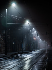 Street lights foggy misty night. Tram route on a city street.
