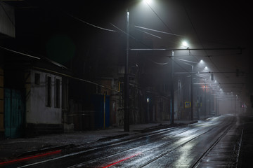 Street lights foggy misty night. Tram route on a city street.
