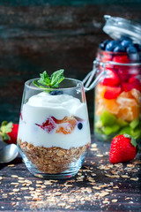Healthy breakfast - yogurt, muesli, berries and fruits in glass jar. Dark rustic style.