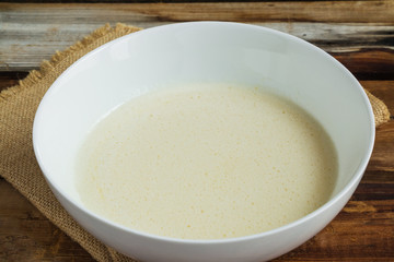 Smooth whisked dough in a white bowl on wooden rustic table closeup.