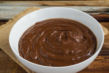 Chocolate smooth whisked dough in a white bowl on wooden rustic table closeup.