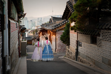 Back of two women wearing hanbok walking through the traditional style houses of Bukchon Hanok Village in Seoul, South Korea.