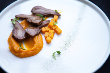 beef tongue cut into pieces with pieces of orange pumpkin lies on a white plate 