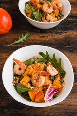 Light fruit salad with fried prawns, persimmon, arugula and walnuts in white bowls on wooden rustic table