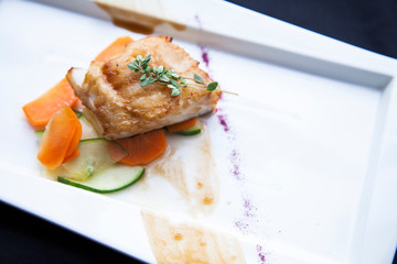 baked fish on a pillow of vegetables on a white plate decorated with purple powder