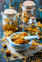Bottles and dried calendula officinalis petals with macerated oil on wooden background.