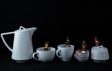 A few cups, a teapot and a sugar bowl, spoons on a black background.