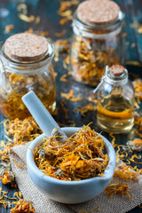 Bottles and dried calendula officinalis petals with macerated oil on wooden background.
