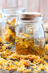 Bottles and dried calendula officinalis petals with macerated oil on wooden background.
