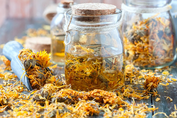Bottles and dried calendula officinalis petals with macerated oil on wooden background. - obrazy, fototapety, plakaty