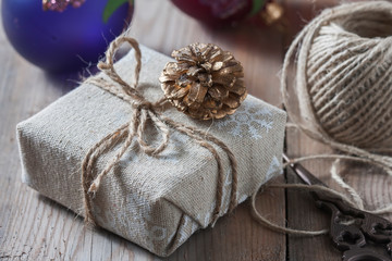 Fototapeta na wymiar Gift box wrapped linen cloth and decorated with cord, jute, christmas decoration on brown vintage wooden boards background.