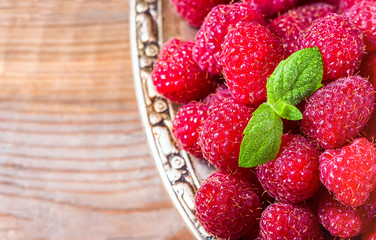 Ripe sweet raspberries in bowl on wooden table, closeup.
