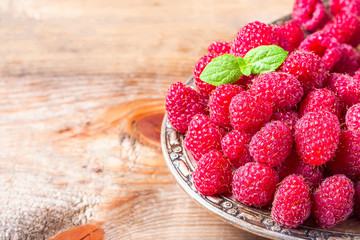 Ripe sweet raspberries in bowl on wooden table, closeup.