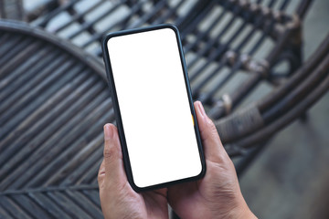 Top view mockup image of hands holding black mobile phone with blank white screen in outdoor