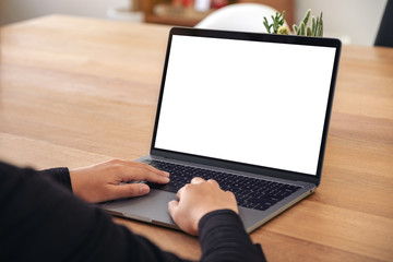 Mockup image of hands using and typing on laptop with blank white desktop screen on wooden table in office