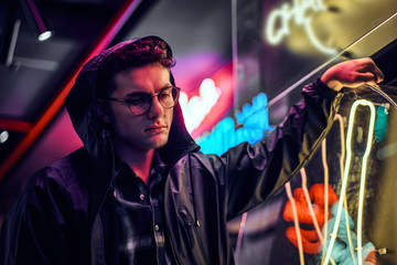 A pensive young man leaning on an illuminated signboard in the street at night.