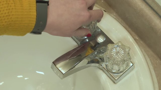 A woman's hand turns on and off the hot water on a bathroom sink faucet.