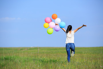 Young asian woman running and jumping with colored balloons outdoors