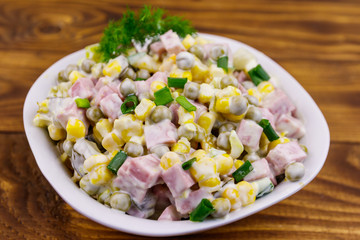 Tasty salad with sausage, green pea, canned corn, bell pepper, cucumber and mayonnaise on wooden table