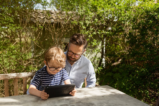 Mid adult man and boy use a device at an outdoor table in Sweden