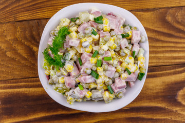 Tasty salad with sausage, green pea, canned corn, bell pepper, cucumber and mayonnaise on wooden table. Top view