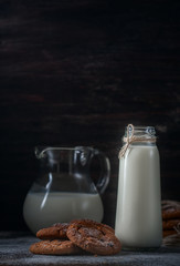 Oatmeal cookies with raisins, chocolate and milk in bottles, wood background