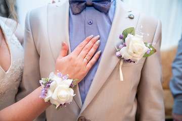 Wedding boutonniere on suit of groom and bride’s hand - obrazy, fototapety, plakaty