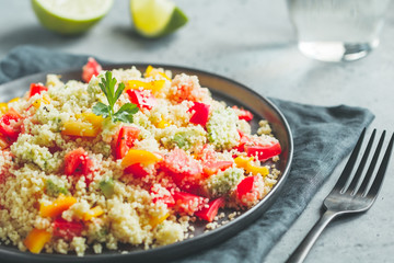 Couscous salad with fresh red and yellow bell peppers, avocado, tomatoes and lime. The concept of vegetarian and healthy food.